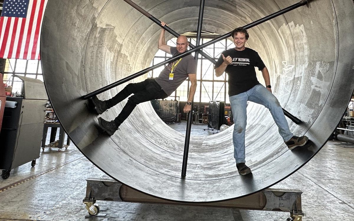 Two people standing inside an 11-foot-diameter steel tube resting on a welded steel stand
